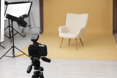 Photo of Camera on tripod, armchair and professional lighting equipment in modern photo studio, space for text