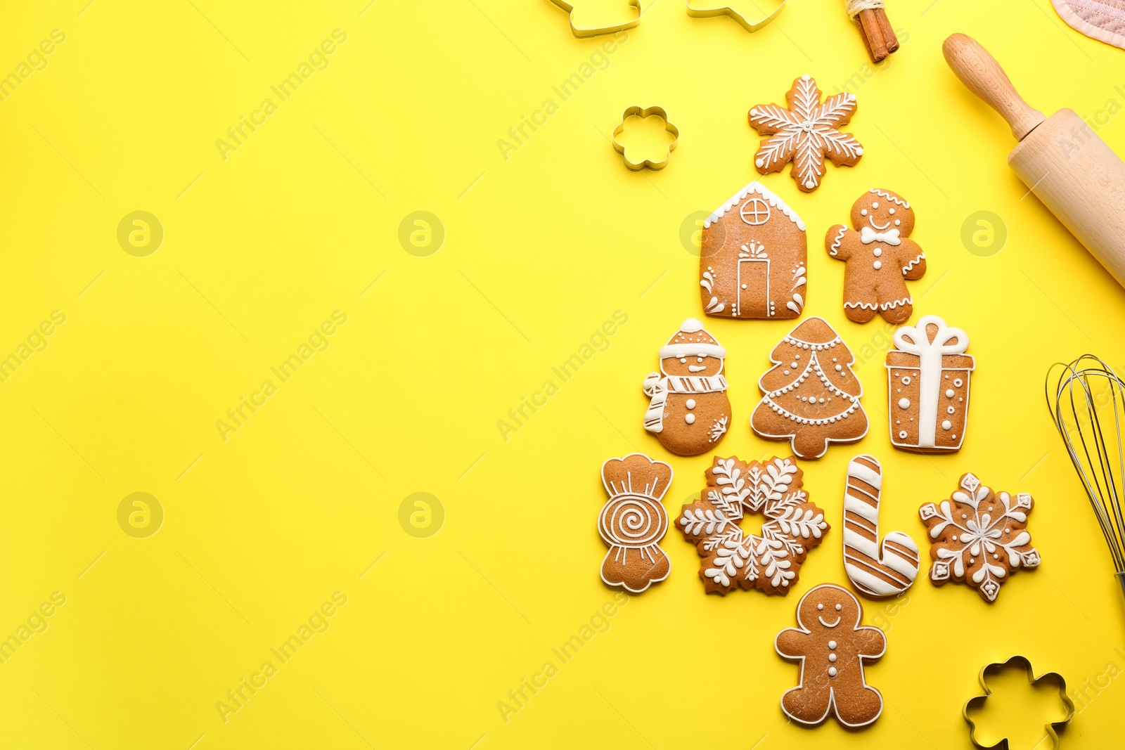 Photo of Kitchen utensils near Christmas tree shape made of delicious gingerbread cookies on yellow background, flat lay. Space for text