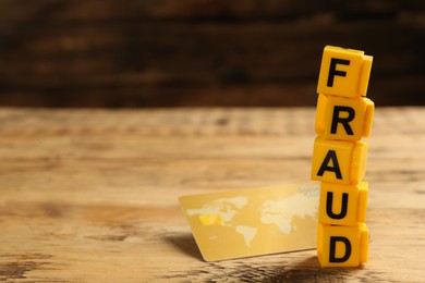 Photo of Word Fraud of yellow cubes with letters and credit card on wooden background. Space for text