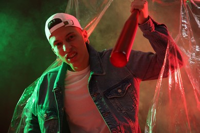 Photo of Young man with baseball bat on color background in neon lights