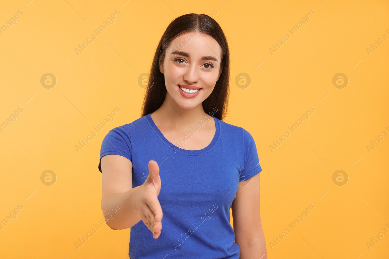 Photo of Happy young woman welcoming and offering handshake on yellow background