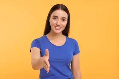 Happy young woman welcoming and offering handshake on yellow background