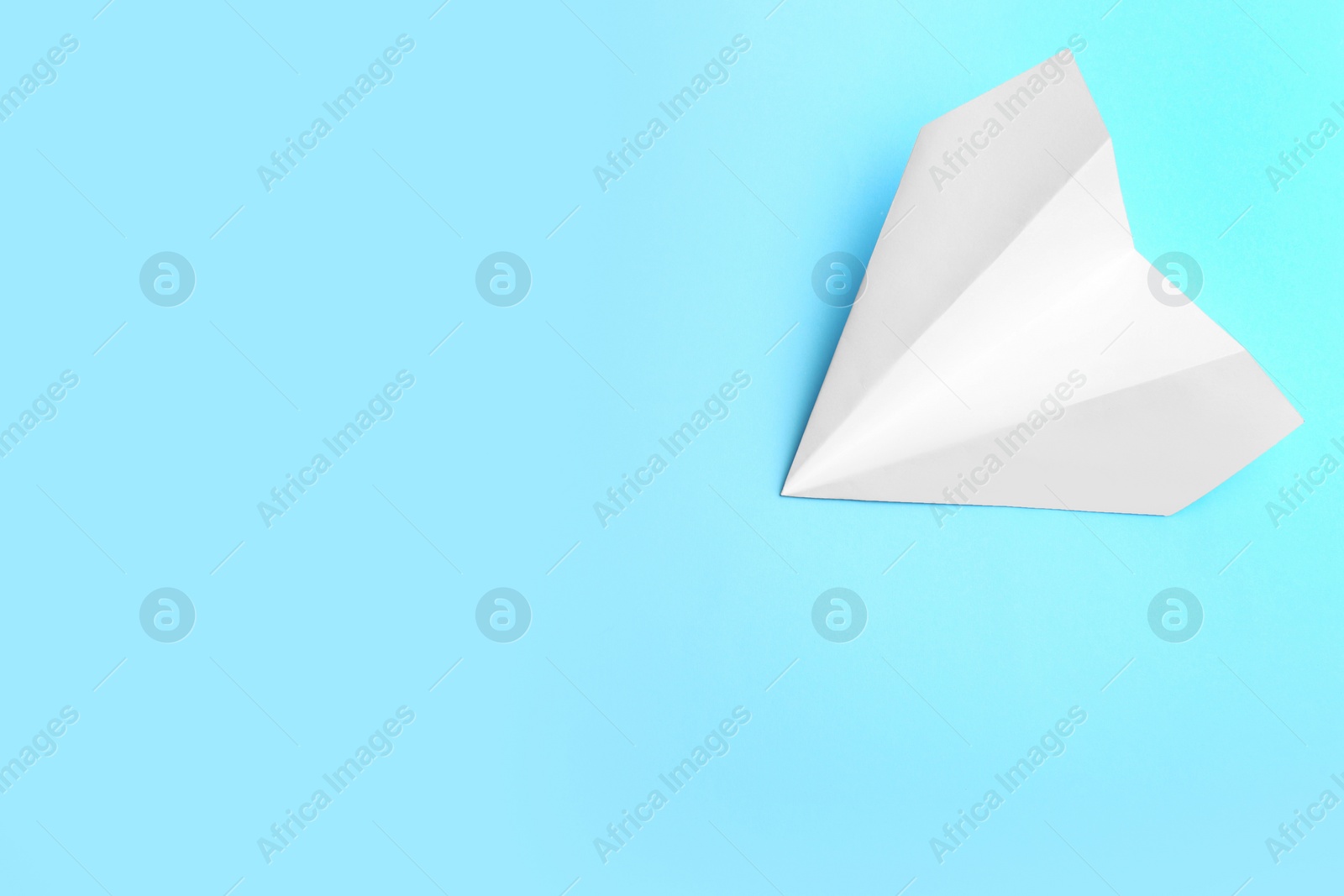 Photo of White paper plane on light blue background, top view. Space for text