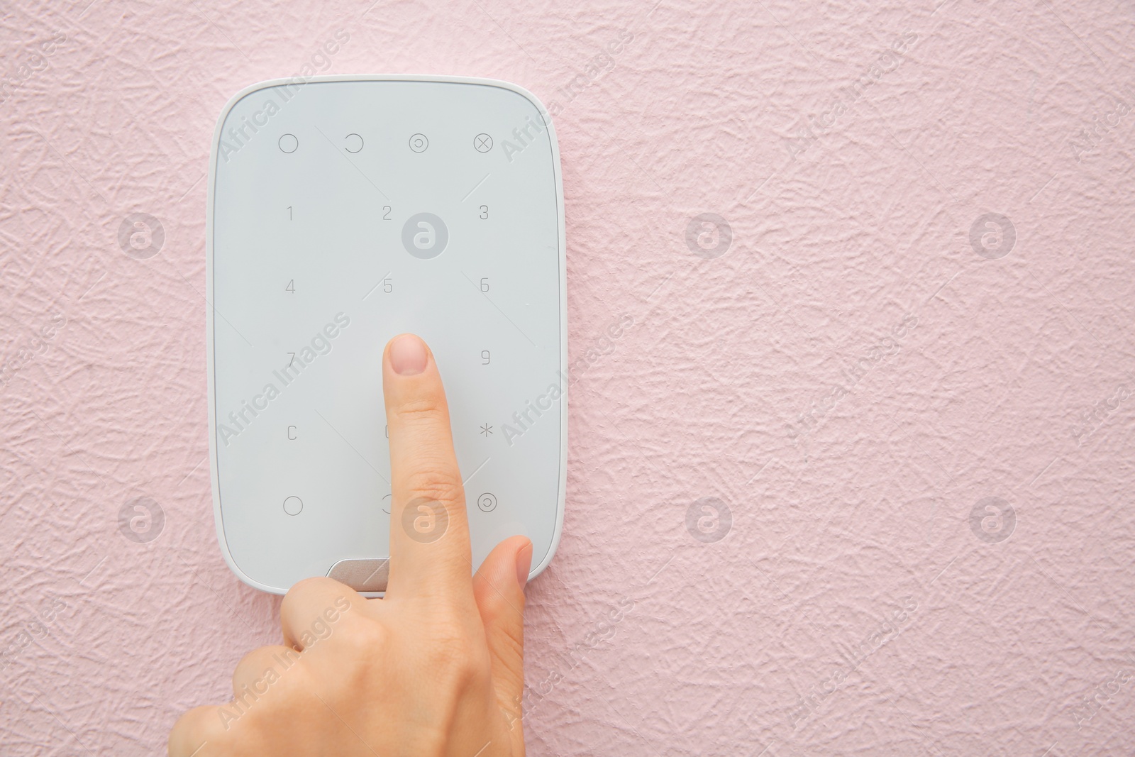 Photo of Young woman entering code on alarm system keypad indoors