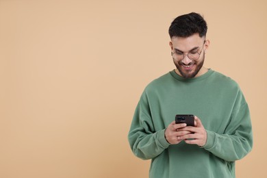 Happy young man using smartphone on beige background, space for text