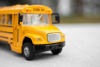 Photo of Yellow toy school bus against blurred background, closeup. Transport for students