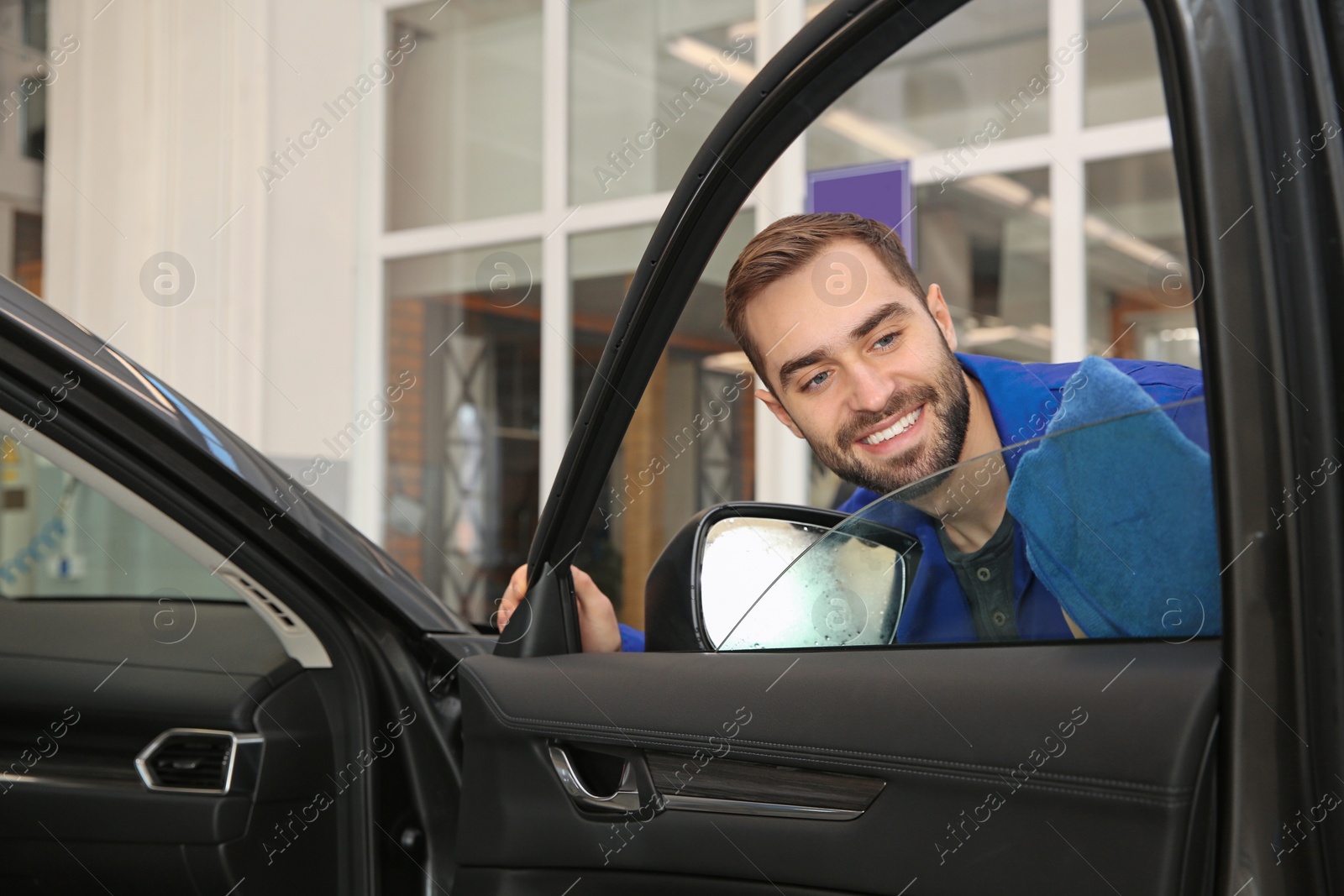 Photo of Worker cleaning automobile window glass with rag at car wash