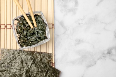 Chopped nori sheets with chopsticks on white marble table, top view. Space for text