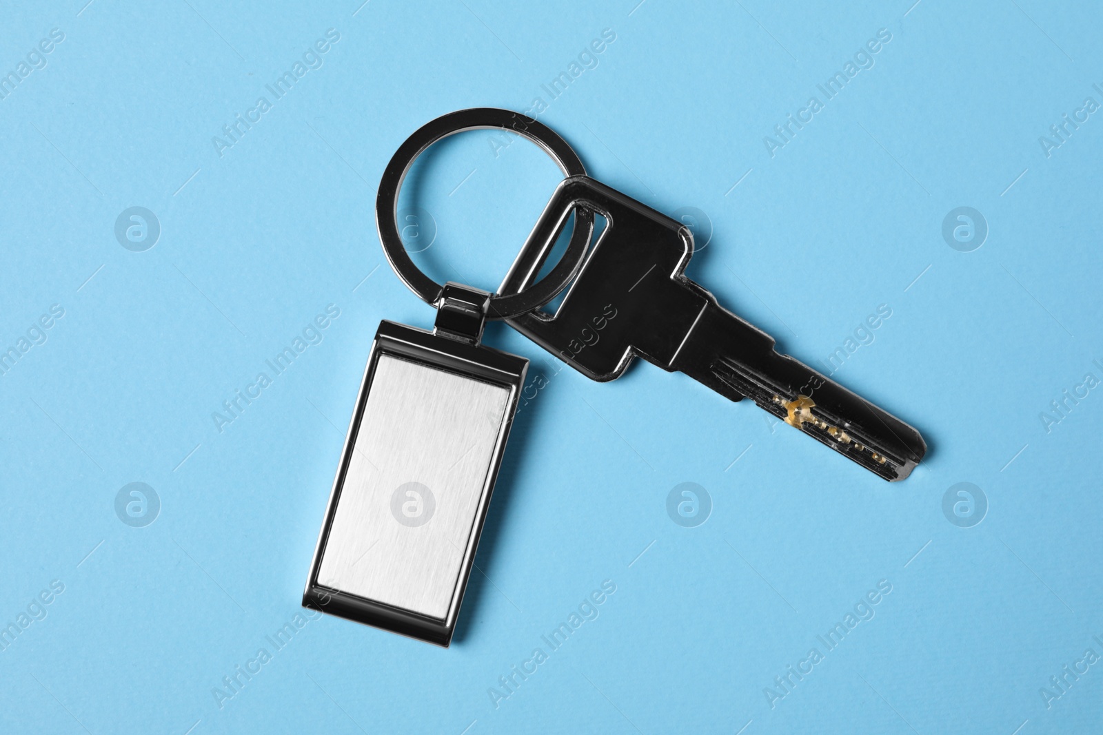 Photo of Key with metallic keychain on light blue background, top view