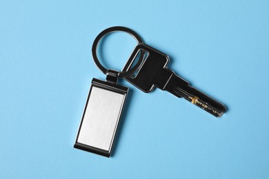 Key with metallic keychain on light blue background, top view