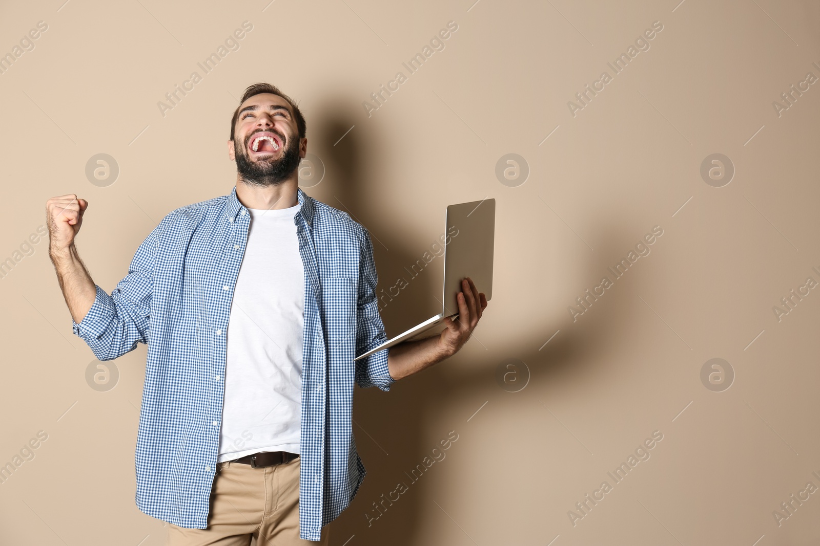 Photo of Emotional young man with laptop celebrating victory on color background. Space for text