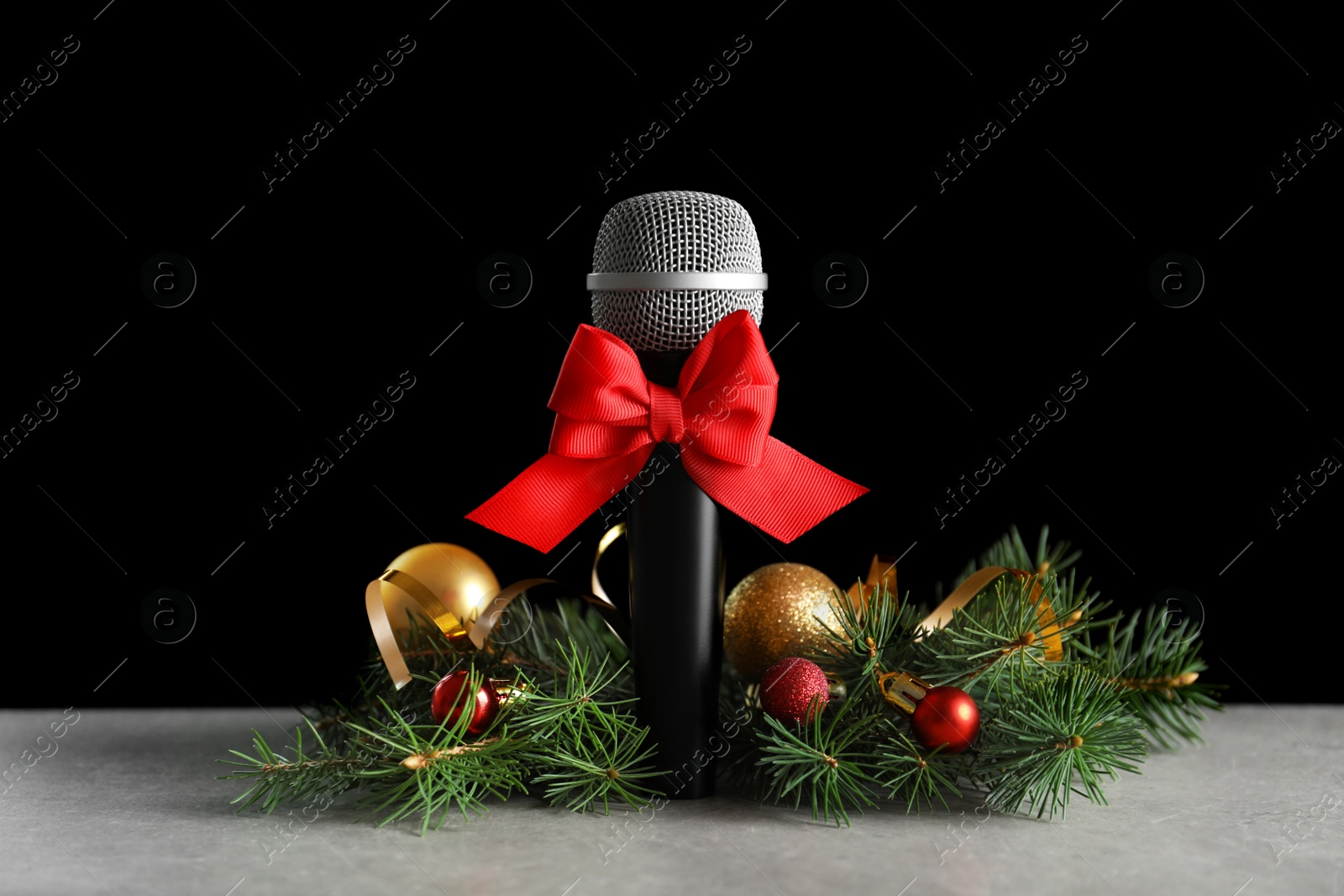 Photo of Microphone with bow and decorations on table against black background. Christmas music concept