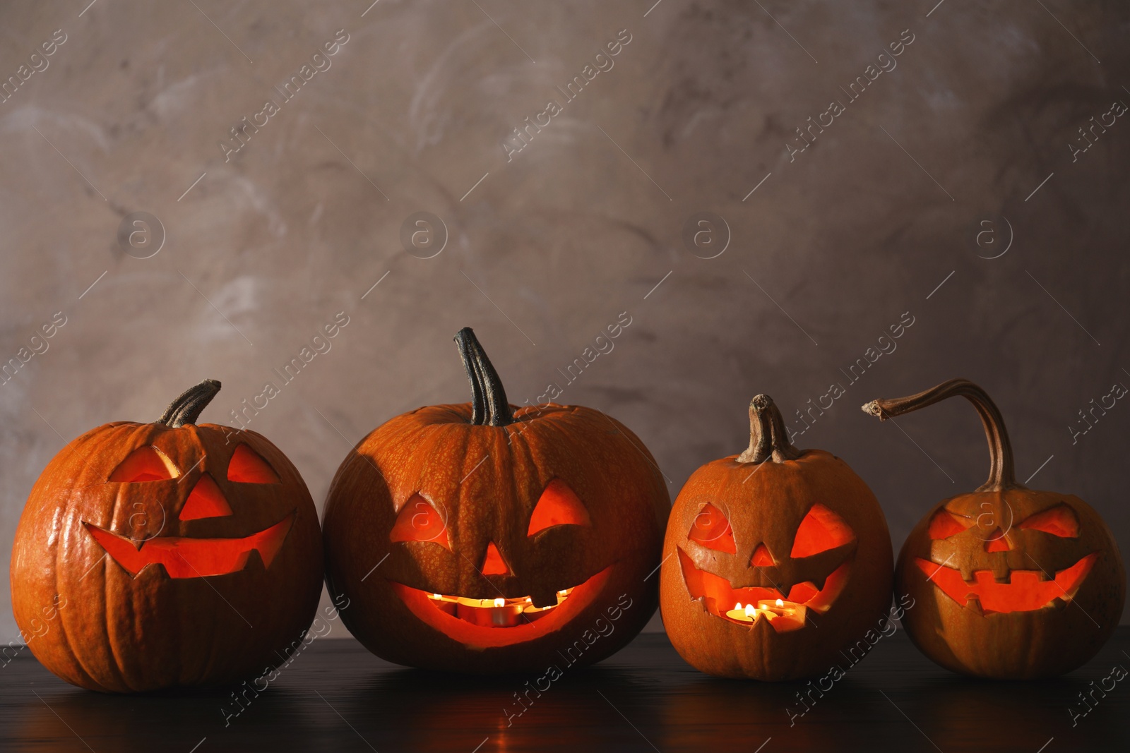 Photo of Halloween pumpkin head jack lanterns on table against color background