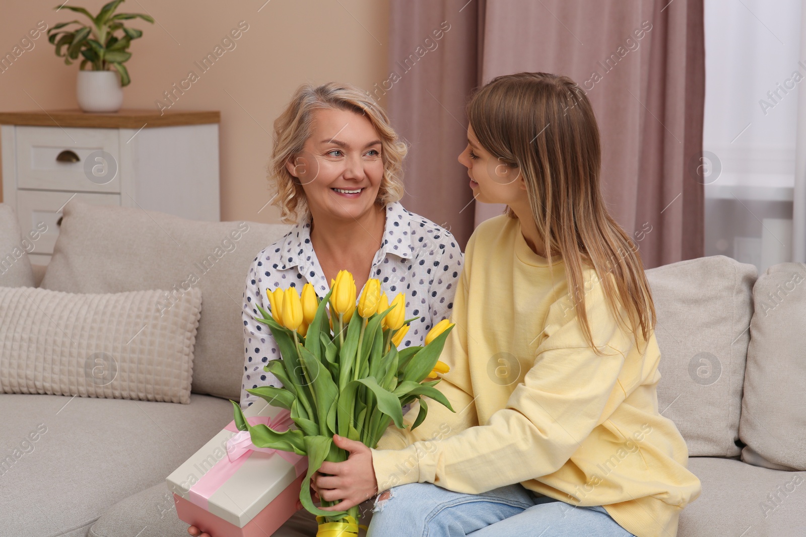 Photo of Young daughter congratulating her mom with flowers and gift at home. Happy Mother's Day