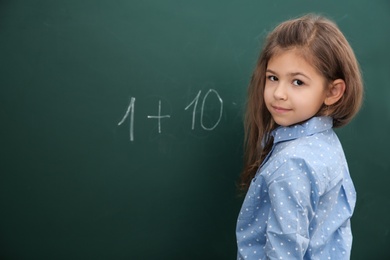 Photo of Little child solving math sum near chalkboard