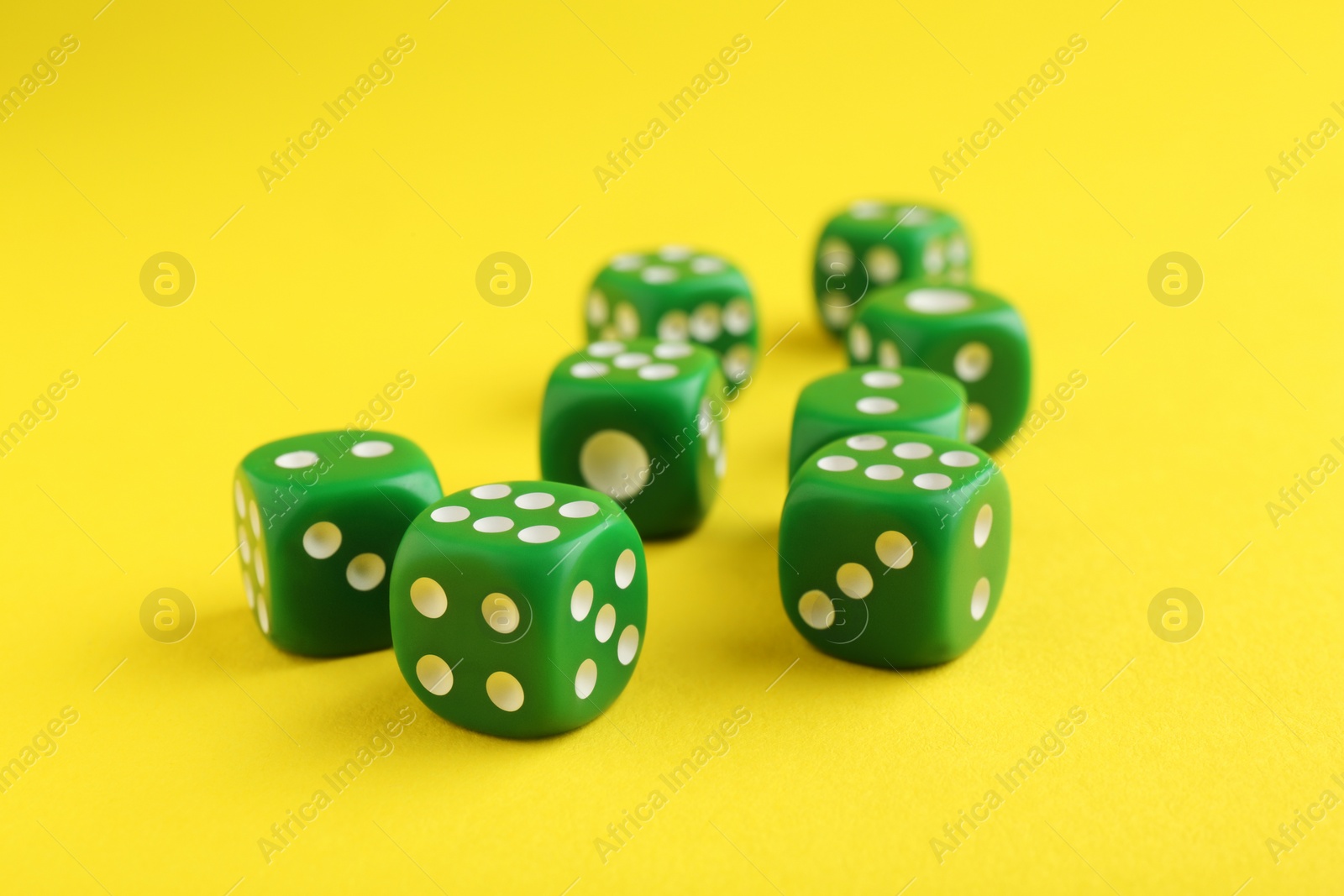 Photo of Many green game dices on yellow background, closeup