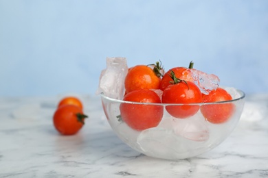 Photo of Bowl with frozen cherry tomatoes and ice cubes on marble table. Keeping vegetables fresh