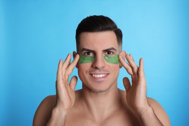 Photo of Man applying green under eye patches on light blue background