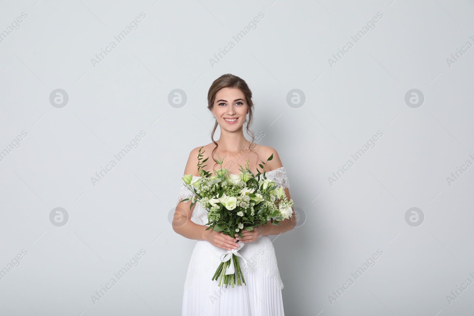 Photo of Young bride wearing wedding dress with beautiful bouquet on light grey background