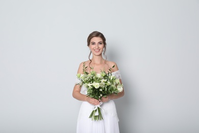 Photo of Young bride wearing wedding dress with beautiful bouquet on light grey background