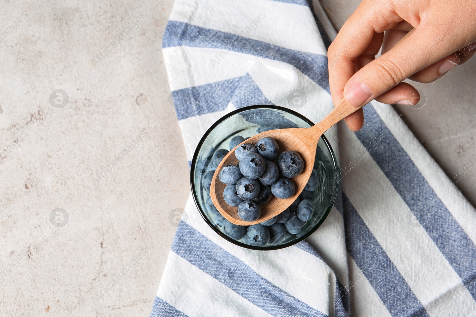 Photo of Woman holding spoon with juicy blueberries over glass on color table, top view. Space for text