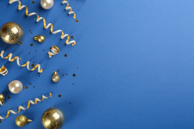 Photo of Shiny serpentine streamers and Christmas balls on blue background, flat lay. Space for text