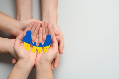 Image of People holding paper family cutout in colors of Ukrainian flag on light background, top view. Space for text