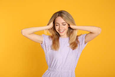 Portrait of beautiful young woman with blonde hair on yellow background