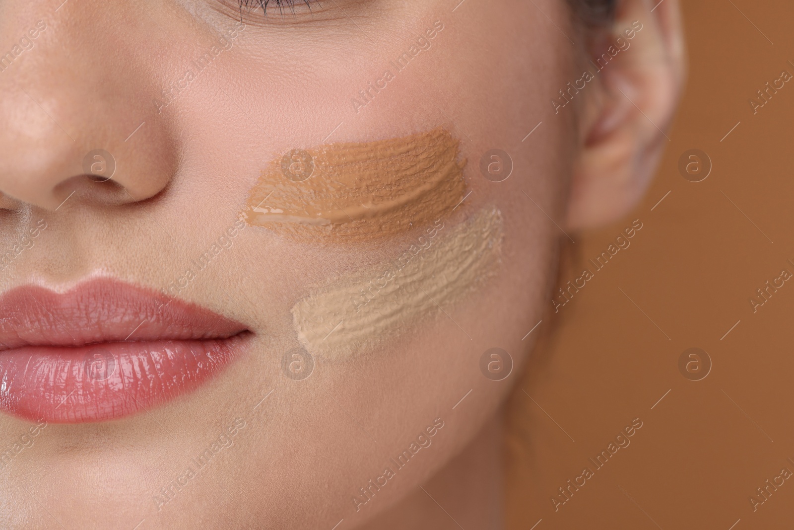 Photo of Woman with swatches of foundation on face against brown background, closeup