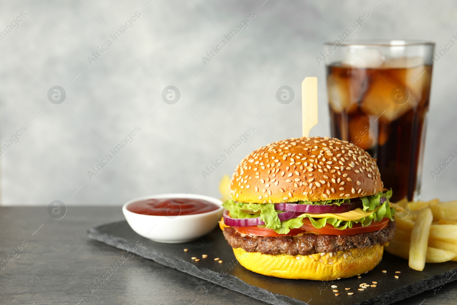 Burger with delicious patty, soda drink, french fries and sauce on dark table against gray background, space for text Photo of Burger with delicious patty, soda drink, french fries and sauce on dark table against gray background, space for text