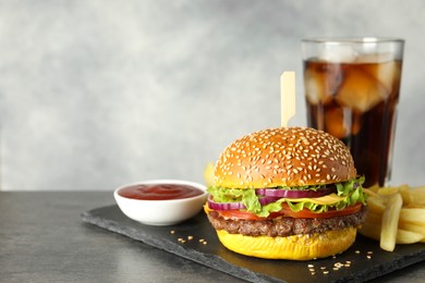 Photo of Burger with delicious patty, soda drink, french fries and sauce on dark table against gray background, space for text