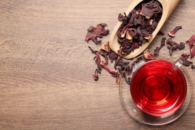 Cup of fresh hibiscus tea and dry flower leaves on wooden table, flat lay. Space for text