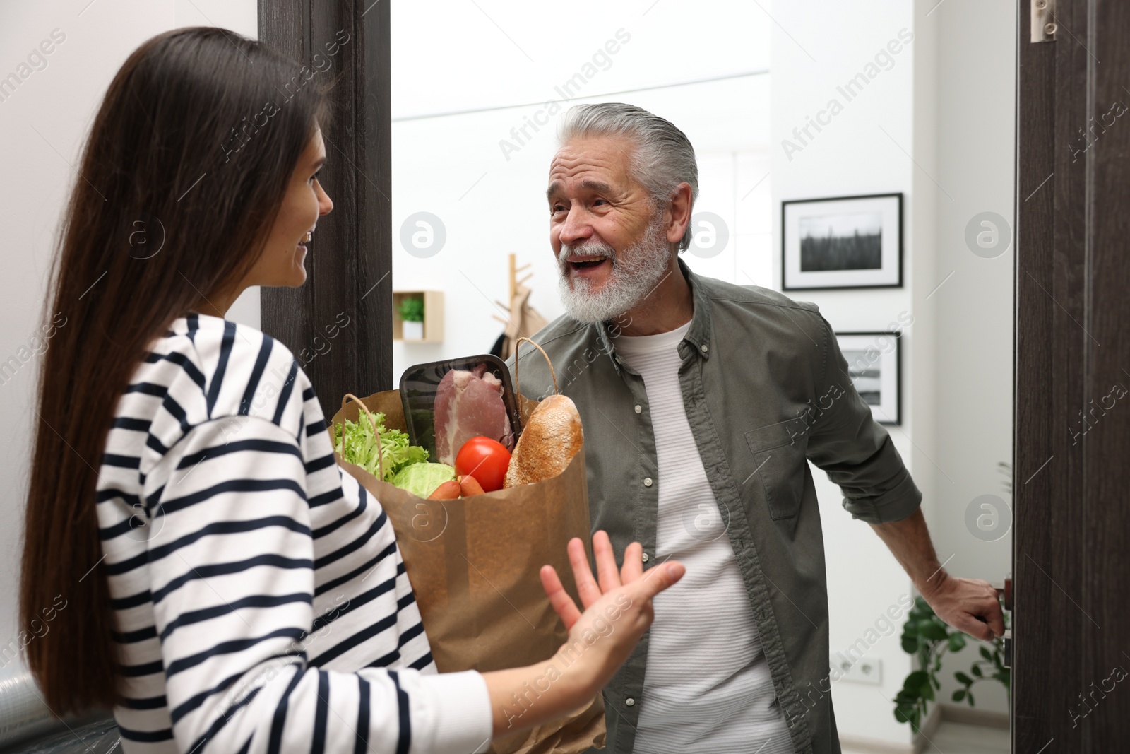 Photo of Courier giving paper bag with food products to senior man indoors