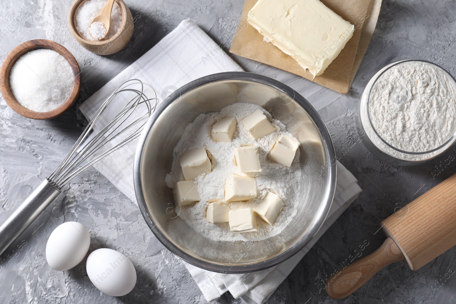 Photo of Making shortcrust pastry. Whisk, rolling pin and different ingredients for dough on grey table, flat lay