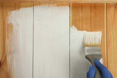 Worker applying white paint onto wooden surface, top view. Space for text