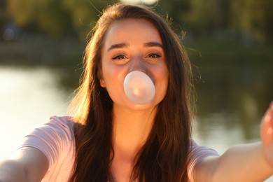 Beautiful young woman blowing bubble gum while taking selfie outdoors