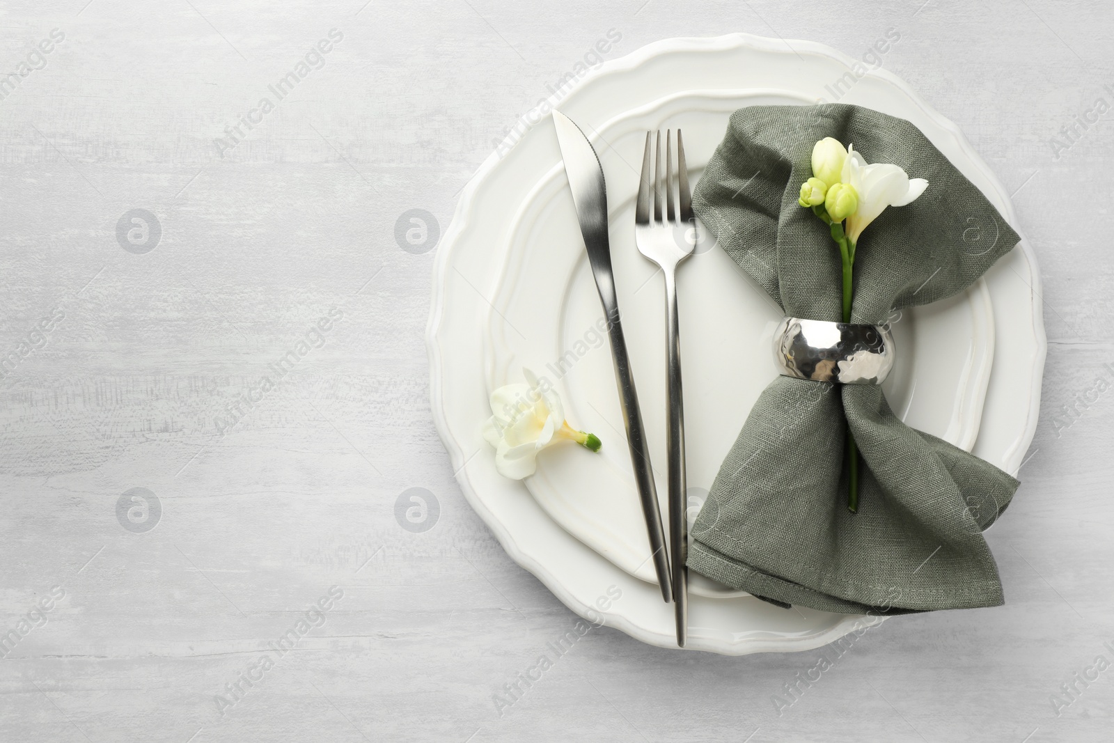 Photo of Stylish setting with cutlery, napkin, flowers and plates on light textured table, top view. Space for text
