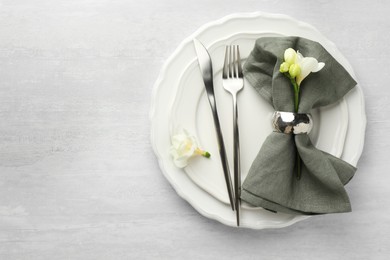 Stylish setting with cutlery, napkin, flowers and plates on light textured table, top view. Space for text