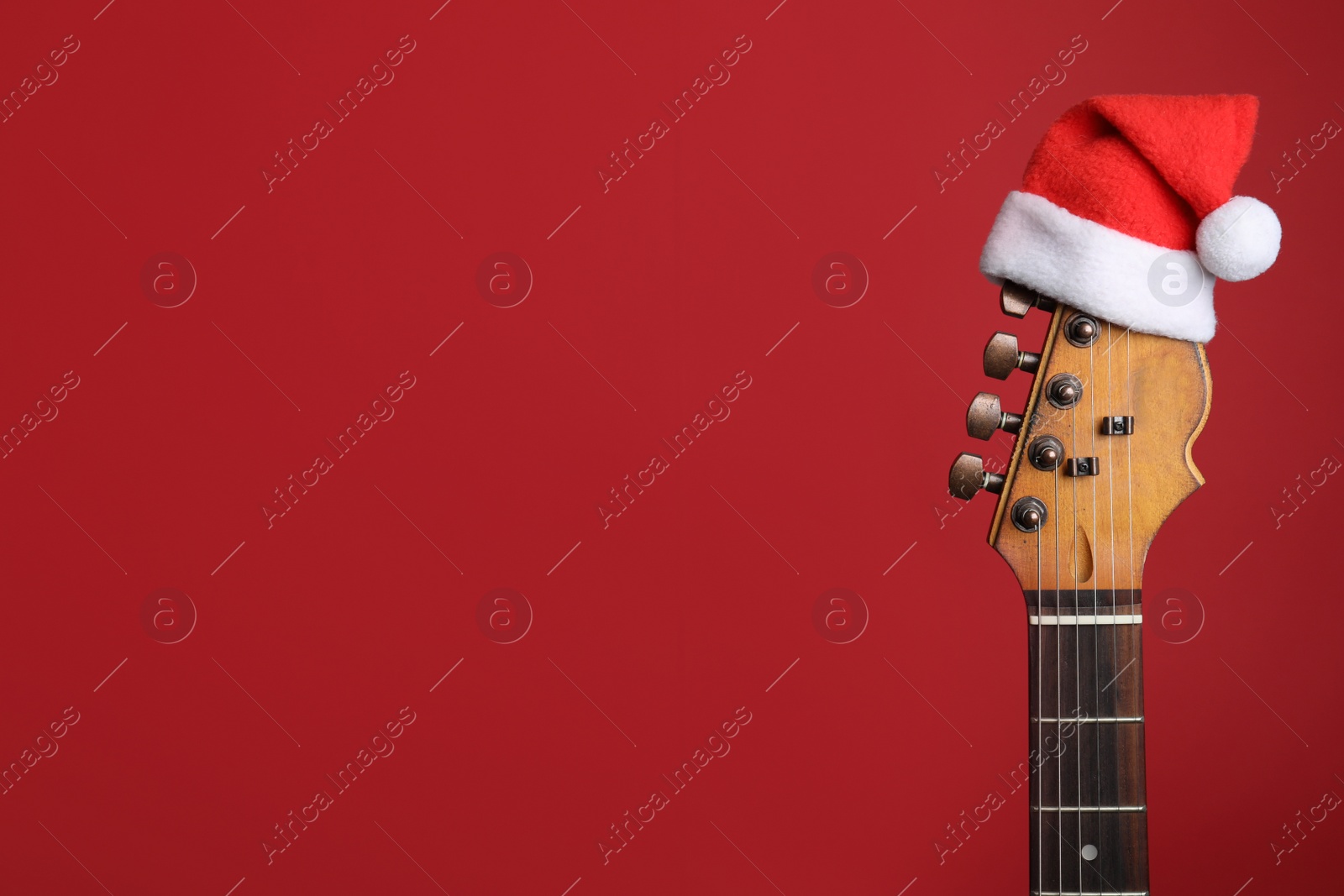 Photo of Guitar with Santa hat on red background, space for text. Christmas music concept