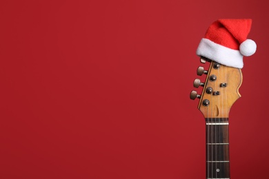 Guitar with Santa hat on red background, space for text. Christmas music concept