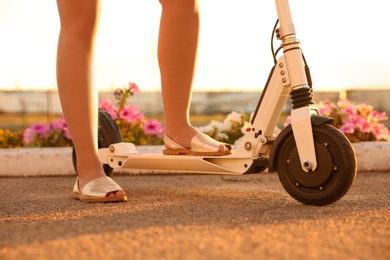 Photo of Woman riding electric kick scooter outdoors on sunny day, closeup