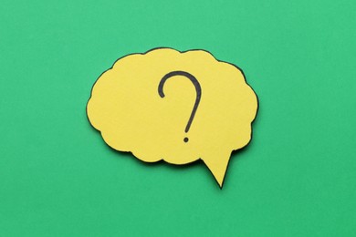 Paper speech bubble with question mark on green background, top view