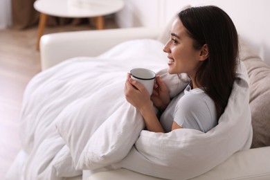 Photo of Woman covered in blanket holding cup of drink on sofa, space for text