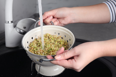 Photo of Woman washing sprouted green buckwheat over sink, closeup