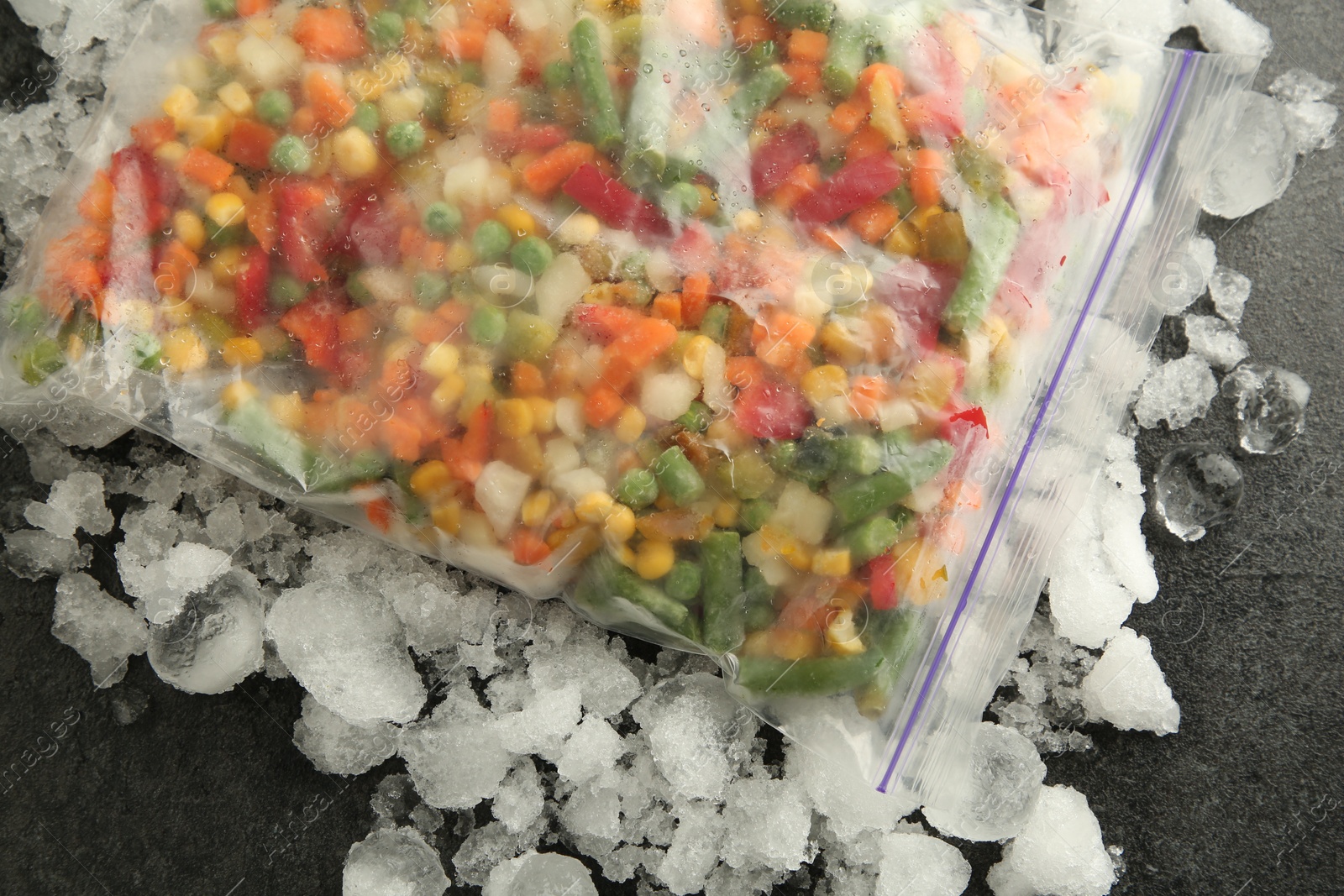 Photo of Zip bag with different frozen vegetables and ice on grey table, top view