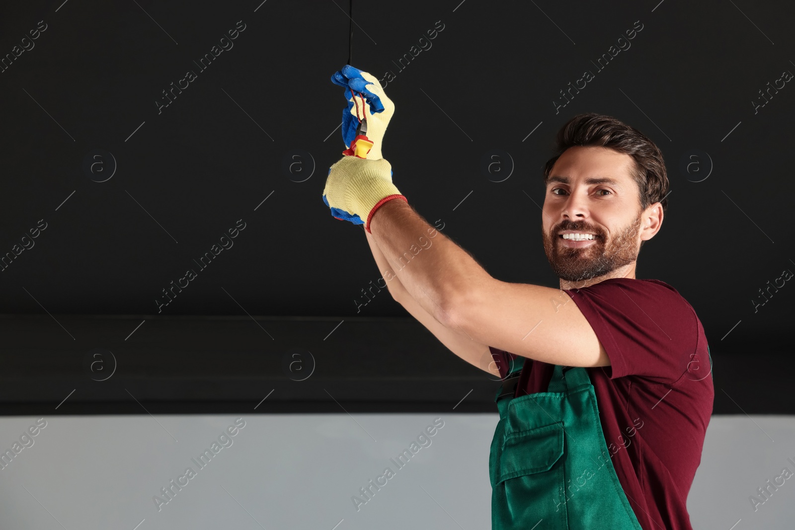 Photo of Electrician with pliers repairing ceiling wiring indoors