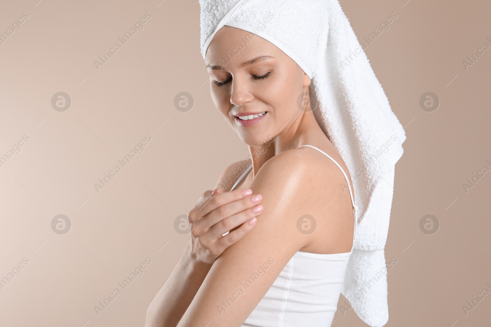 Photo of Happy woman applying body oil onto shoulder on beige background, space for text