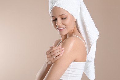 Photo of Happy woman applying body oil onto shoulder on beige background, space for text