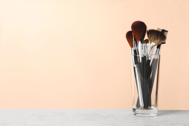 Set of professional makeup brushes on grey table against beige background, space for text