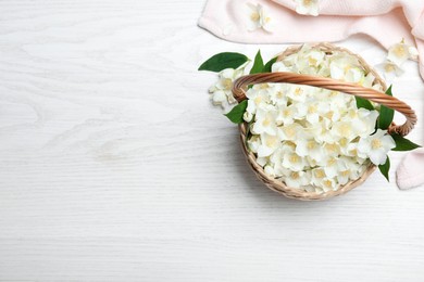 Photo of Beautiful jasmine flowers in wicker basket on white wooden table, flat lay. Space for text